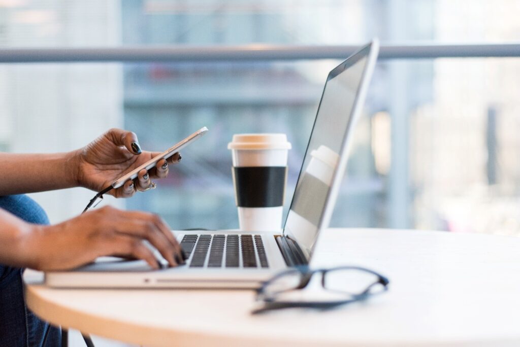 scrivania con pc, occhiali da vista, tazza di caffè americano, mani che lavorano al pc e al telefono