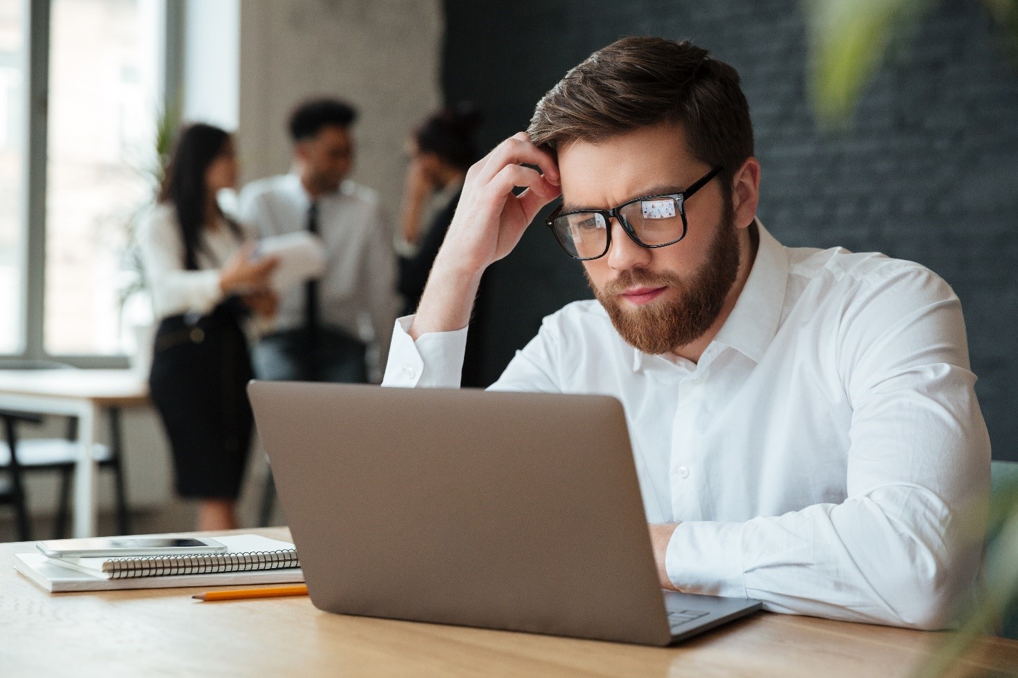 uomo con occhiali in ufficio guarda al pc con espressione confusa